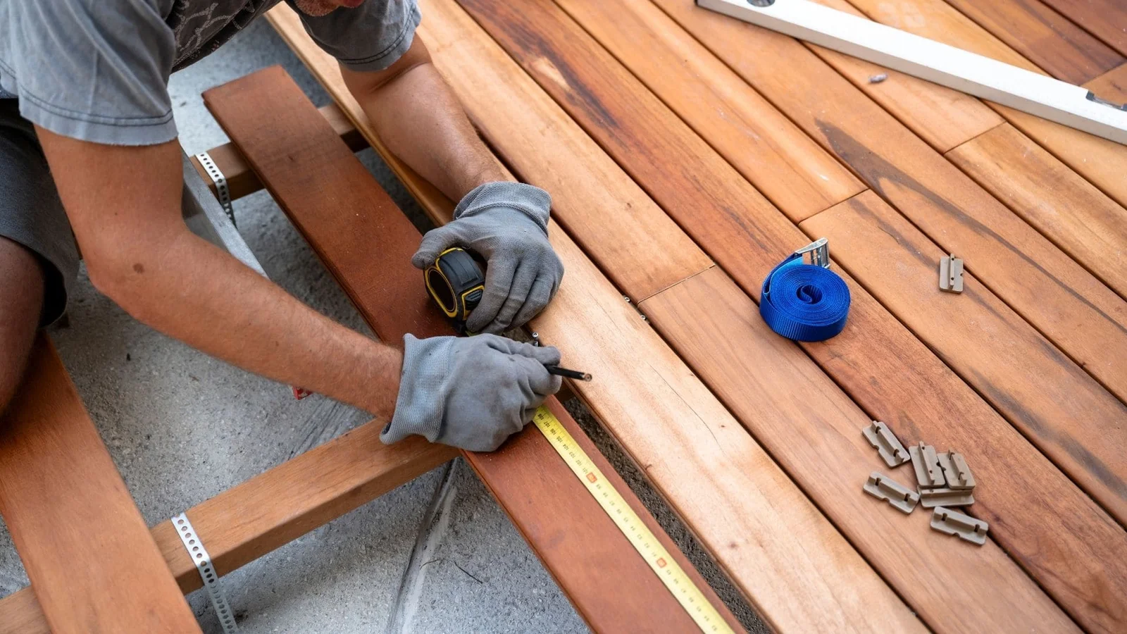 Worker installing wood deck boards with tape measure and stainless steel fasteners