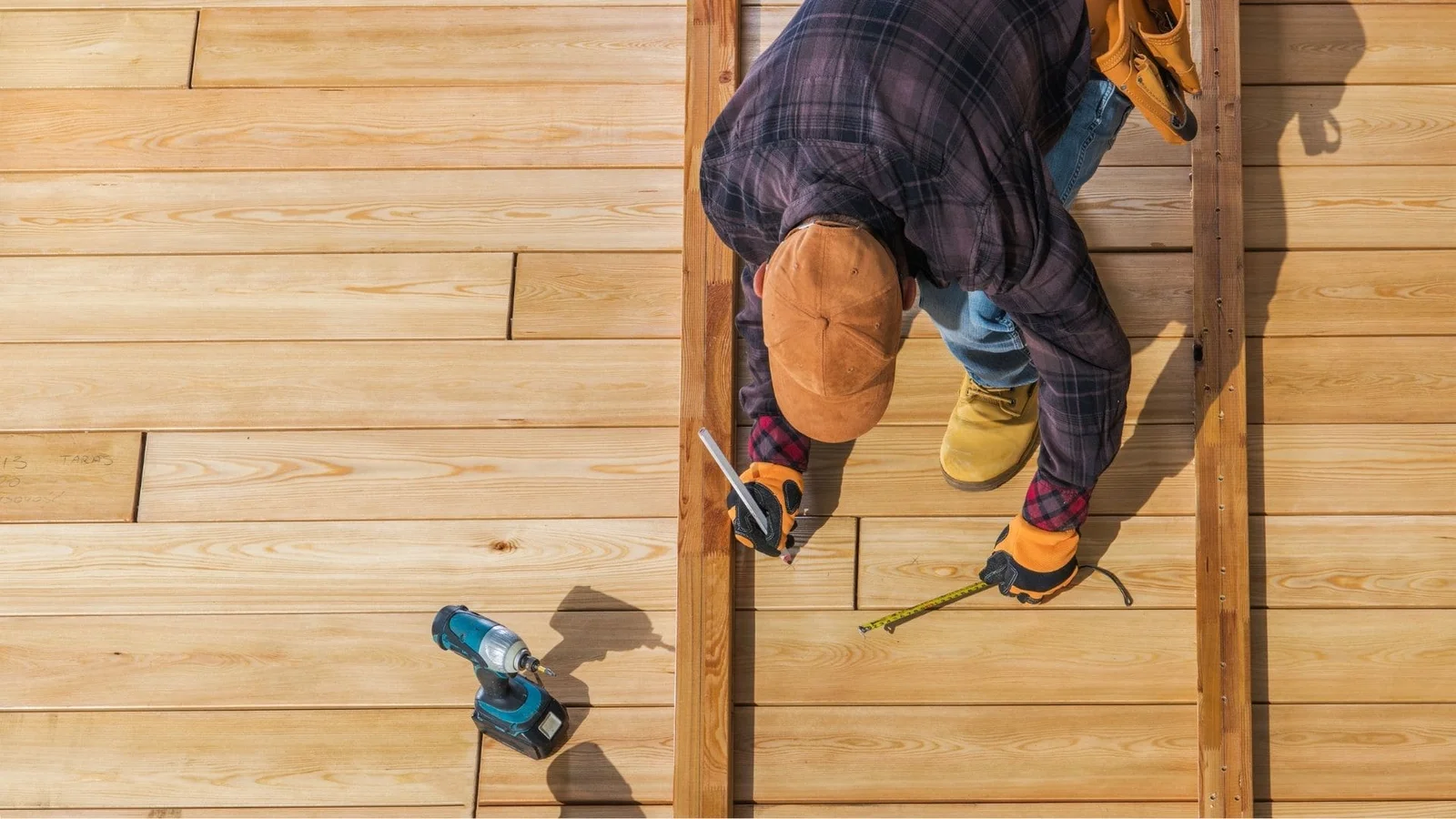 Worker installing hardwood deck boards on wooden frame structure with tools