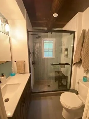 Renovated bathroom with frameless glass shower, dark tile, white vanity, and updated fixtures